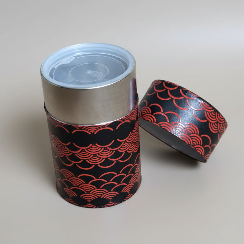 Red and black patterned container with a silver lid on a woven mat